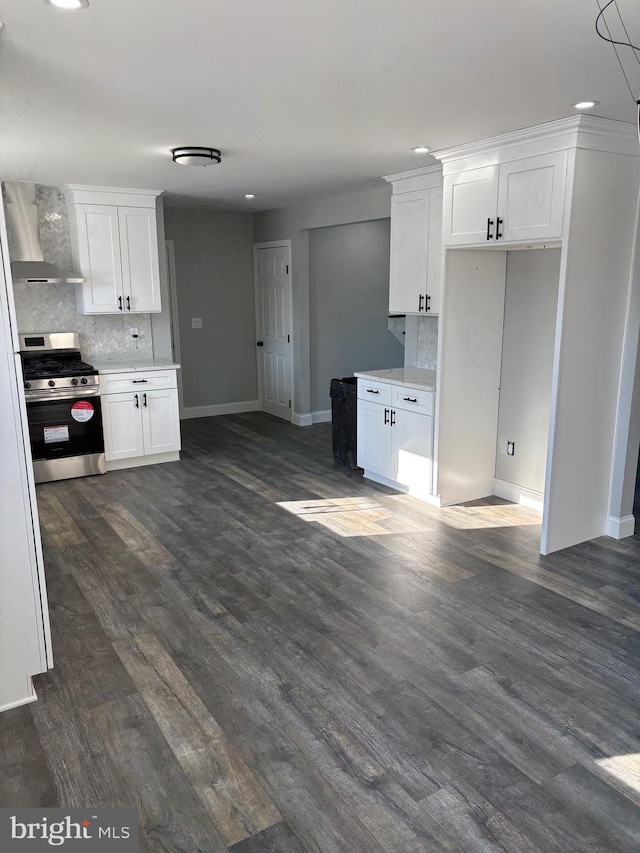 kitchen featuring wall chimney range hood, stainless steel stove, dark hardwood / wood-style floors, white cabinets, and decorative backsplash