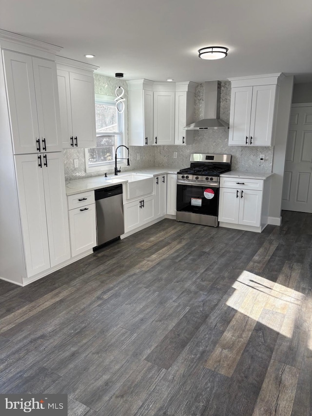 kitchen featuring wall chimney range hood, stainless steel appliances, sink, and white cabinets