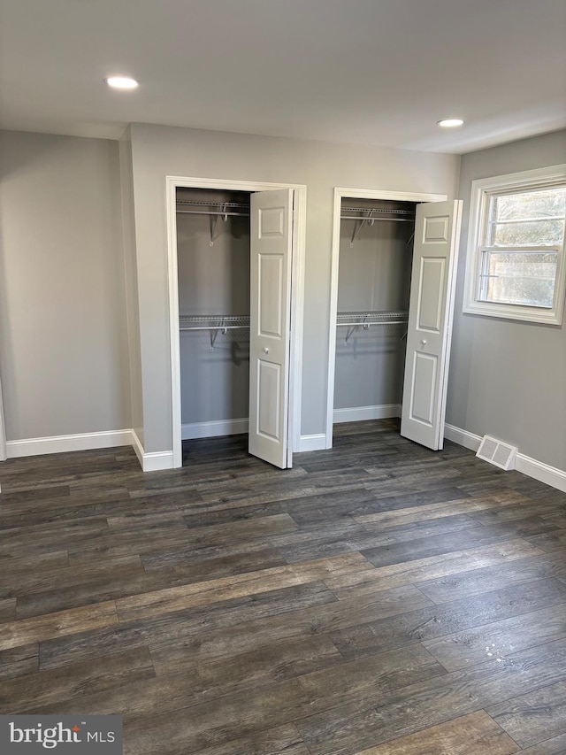 unfurnished bedroom with dark hardwood / wood-style floors and two closets