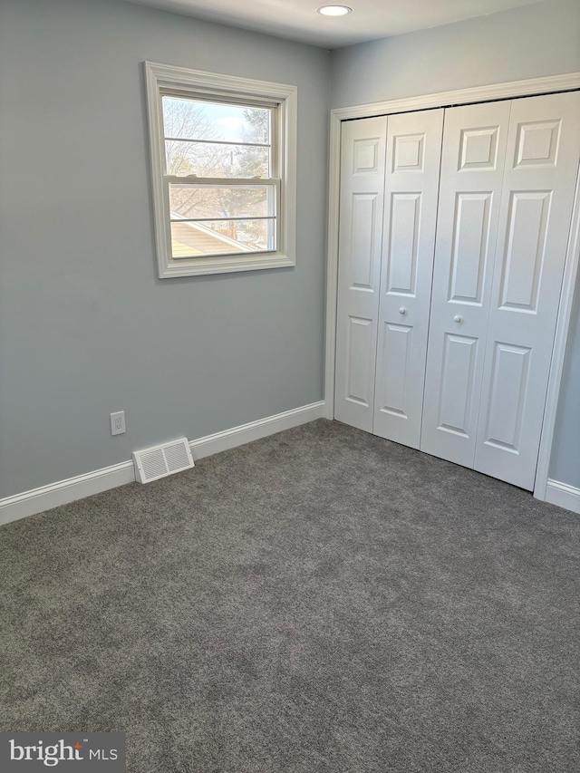 unfurnished bedroom with dark carpet and a closet