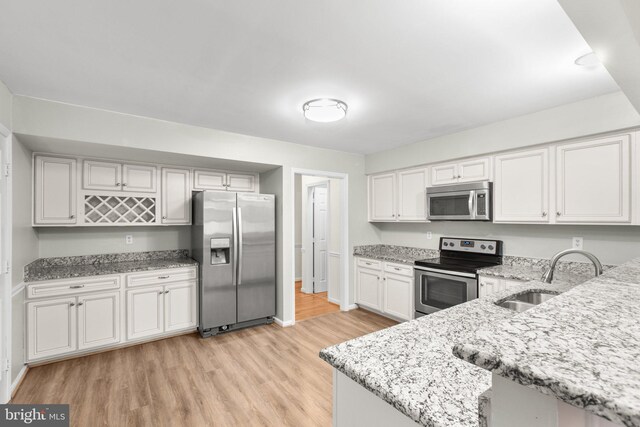 kitchen featuring appliances with stainless steel finishes, light stone counters, sink, light hardwood / wood-style floors, and white cabinetry