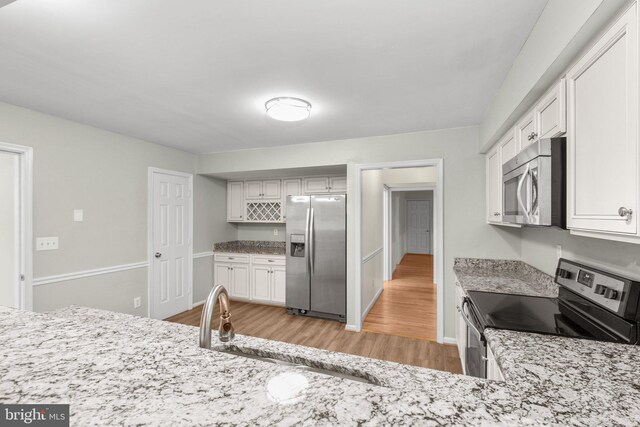 kitchen with light stone countertops, appliances with stainless steel finishes, light wood-type flooring, sink, and white cabinetry