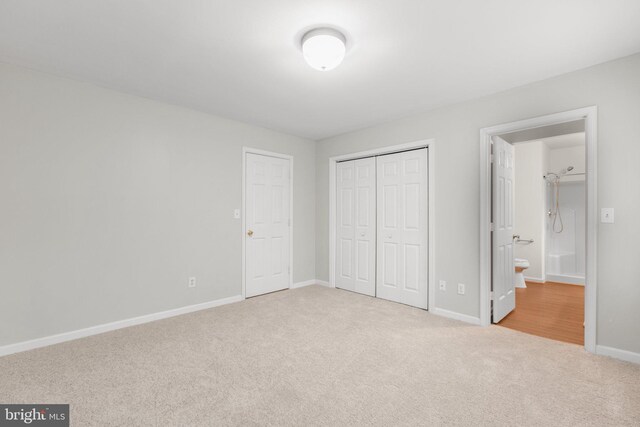 unfurnished bedroom with ensuite bath, a closet, and light colored carpet