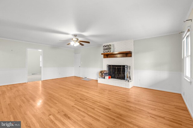 unfurnished living room with ceiling fan, ornamental molding, light wood-type flooring, and a brick fireplace