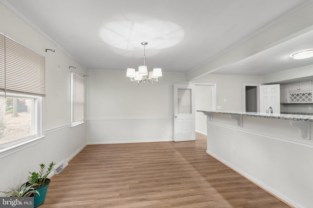 unfurnished dining area featuring an inviting chandelier, ornamental molding, and light hardwood / wood-style flooring