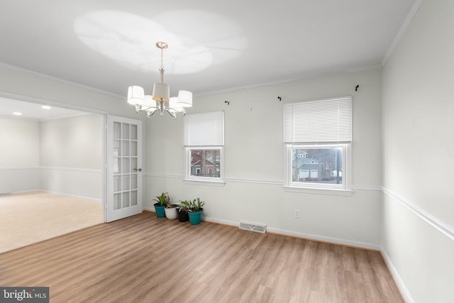 spare room featuring light hardwood / wood-style flooring, ornamental molding, french doors, and a notable chandelier