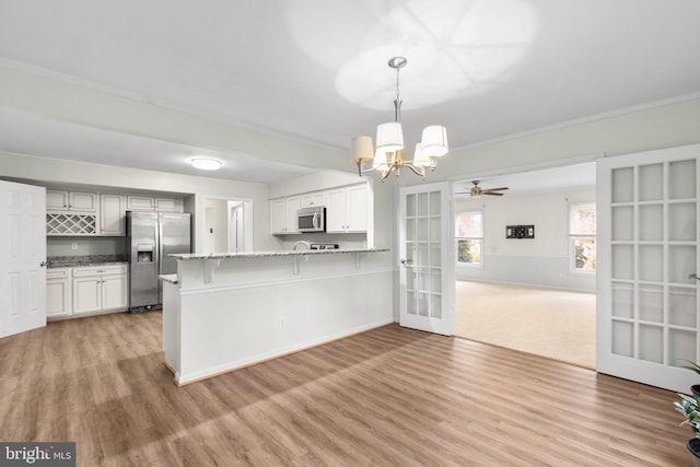 kitchen with kitchen peninsula, appliances with stainless steel finishes, light hardwood / wood-style floors, white cabinetry, and hanging light fixtures