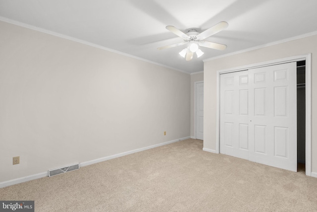 unfurnished bedroom with ceiling fan, light colored carpet, crown molding, and a closet