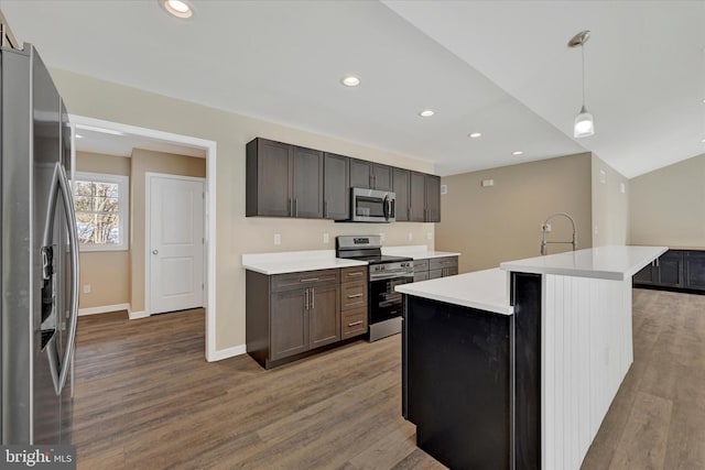 kitchen featuring pendant lighting, hardwood / wood-style flooring, appliances with stainless steel finishes, dark brown cabinetry, and a center island with sink