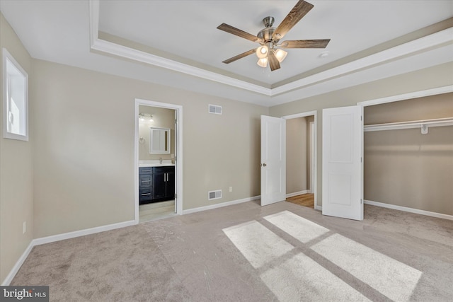 unfurnished bedroom featuring connected bathroom, a raised ceiling, light carpet, and a closet