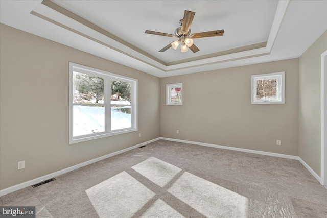 carpeted empty room with ceiling fan and a raised ceiling