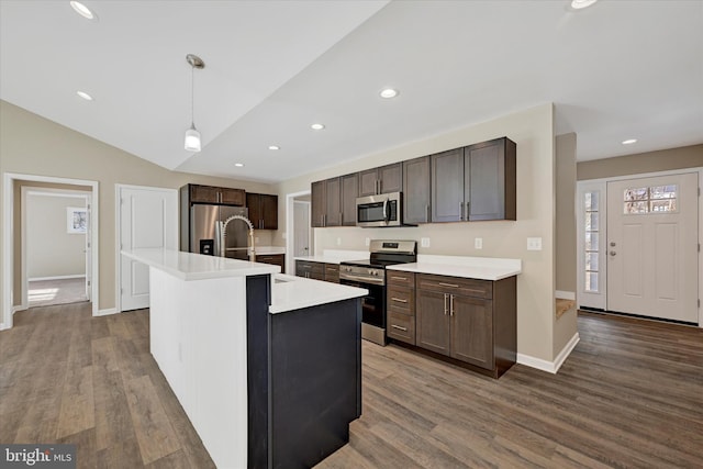 kitchen with vaulted ceiling, pendant lighting, an island with sink, dark hardwood / wood-style flooring, and stainless steel appliances