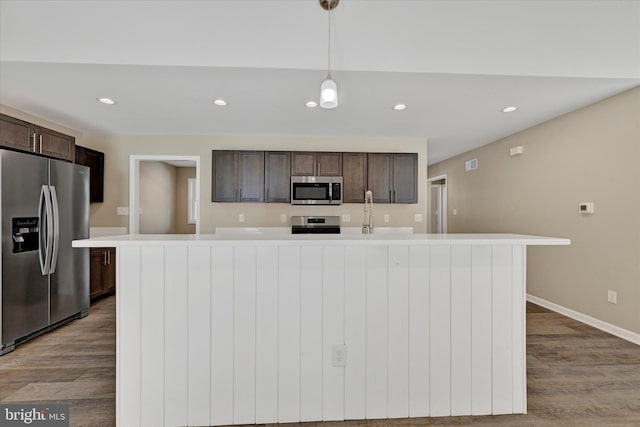 kitchen with dark brown cabinets, a center island with sink, light wood-type flooring, appliances with stainless steel finishes, and pendant lighting