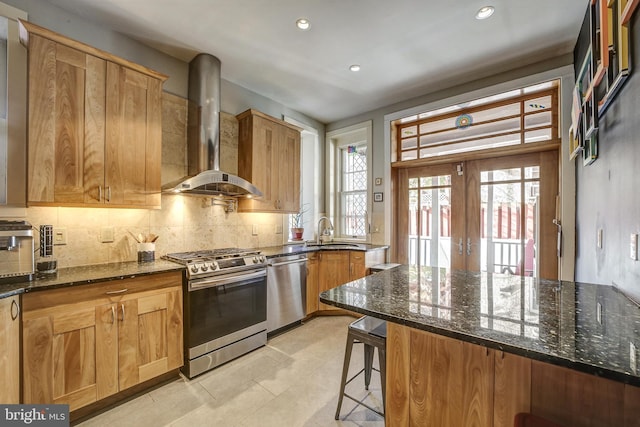 kitchen featuring dark stone countertops, wall chimney exhaust hood, a healthy amount of sunlight, and stainless steel appliances