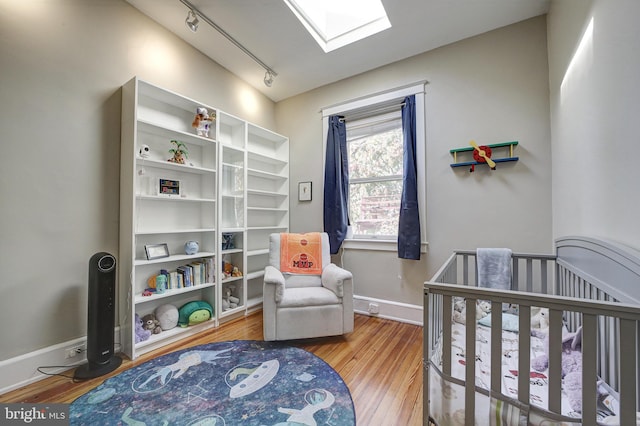 bedroom featuring rail lighting, a nursery area, wood-type flooring, and a skylight