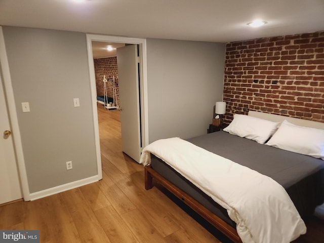 bedroom featuring brick wall and light hardwood / wood-style flooring