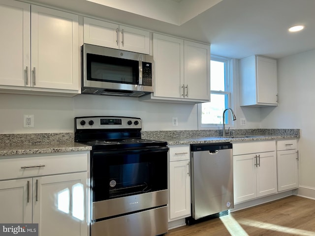 kitchen with white cabinets, sink, appliances with stainless steel finishes, and light hardwood / wood-style flooring