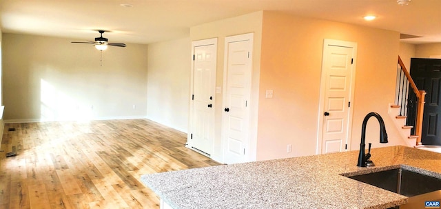 kitchen with light stone countertops, sink, ceiling fan, and light hardwood / wood-style flooring