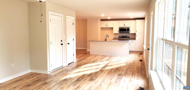 kitchen with light stone counters, sink, white cabinetry, light wood-type flooring, and appliances with stainless steel finishes