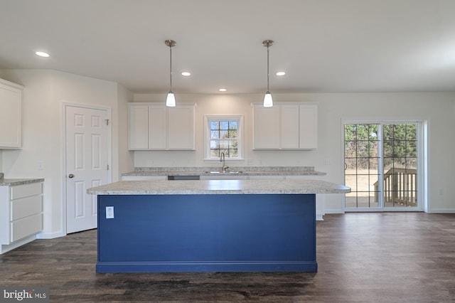 kitchen with dark hardwood / wood-style flooring, hanging light fixtures, sink, a kitchen island, and white cabinetry