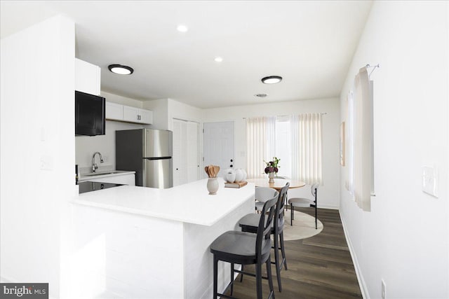 kitchen featuring a kitchen breakfast bar, sink, kitchen peninsula, stainless steel fridge, and white cabinetry