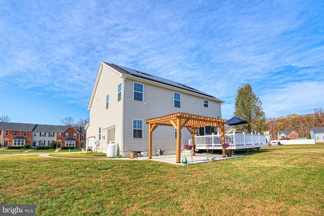 rear view of property featuring a lawn, solar panels, a pergola, and a wooden deck