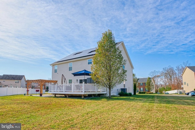 rear view of property featuring a lawn, solar panels, a pergola, and a wooden deck