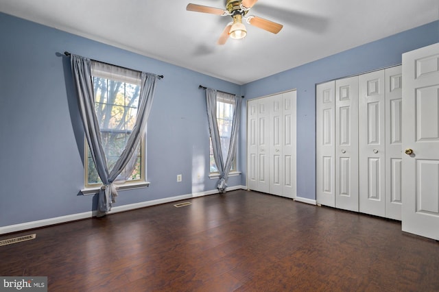 unfurnished bedroom with ceiling fan, dark hardwood / wood-style flooring, multiple closets, and multiple windows