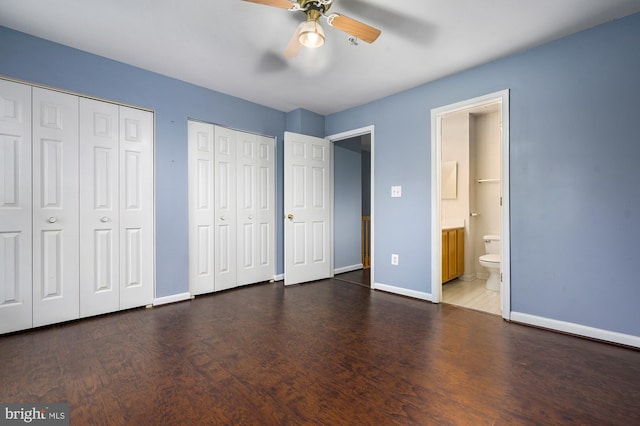 unfurnished bedroom with dark hardwood / wood-style flooring, two closets, ceiling fan, and connected bathroom