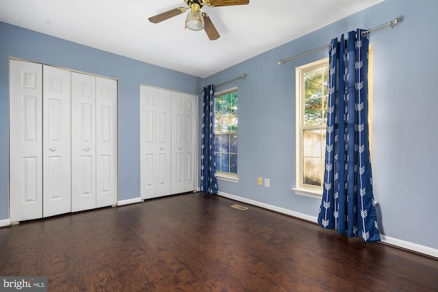 unfurnished bedroom with two closets, ceiling fan, and dark wood-type flooring