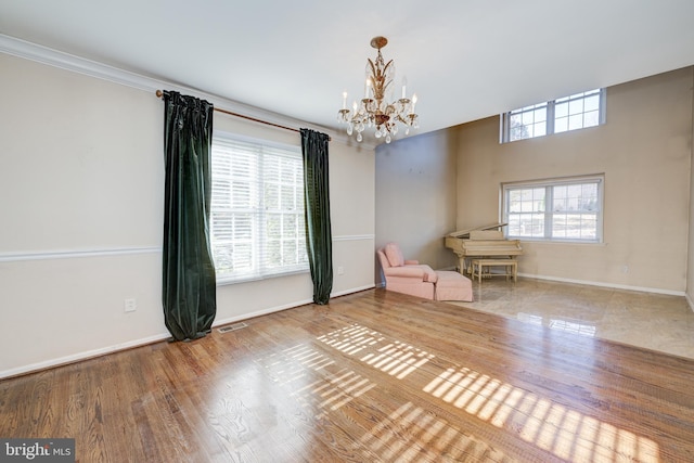 unfurnished room with light wood-type flooring, crown molding, a wealth of natural light, and a notable chandelier