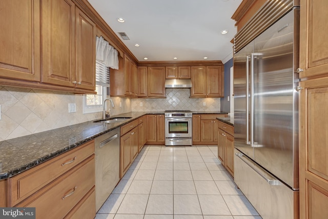 kitchen with sink, decorative backsplash, dark stone countertops, light tile patterned floors, and stainless steel appliances