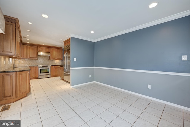 kitchen featuring tasteful backsplash, stainless steel appliances, crown molding, dark stone countertops, and light tile patterned flooring