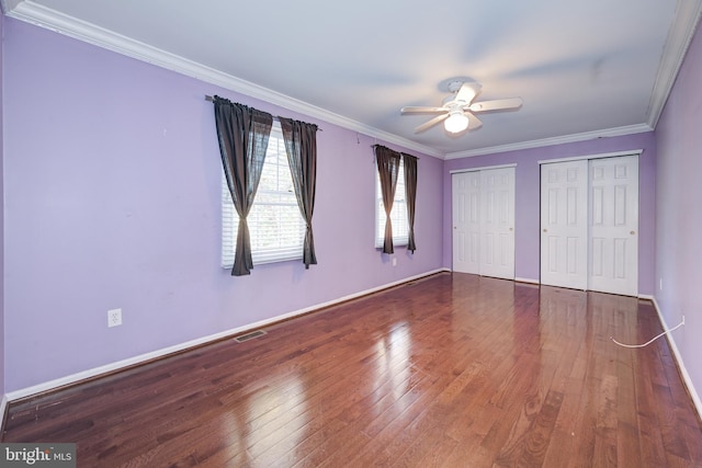 unfurnished bedroom featuring hardwood / wood-style floors, two closets, ceiling fan, and ornamental molding