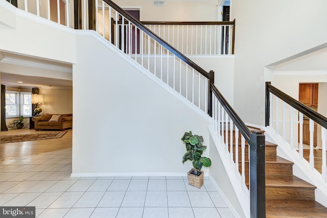 staircase with tile patterned floors, a high ceiling, and ornamental molding