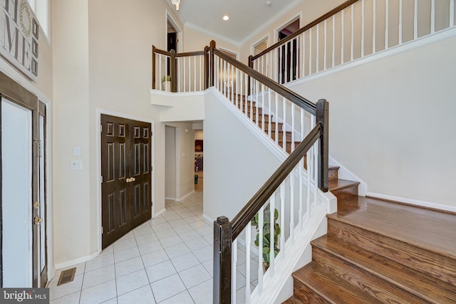 foyer with light wood-type flooring, a towering ceiling, and crown molding