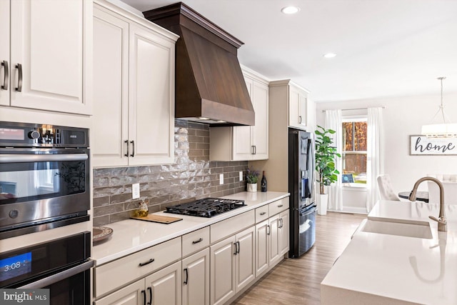 kitchen with sink, appliances with stainless steel finishes, wall chimney exhaust hood, light hardwood / wood-style flooring, and pendant lighting