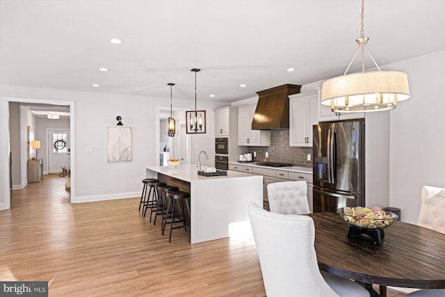 kitchen featuring stainless steel appliances, a kitchen island with sink, decorative light fixtures, and light wood-type flooring