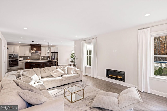 living area featuring a glass covered fireplace, wood finished floors, baseboards, and recessed lighting