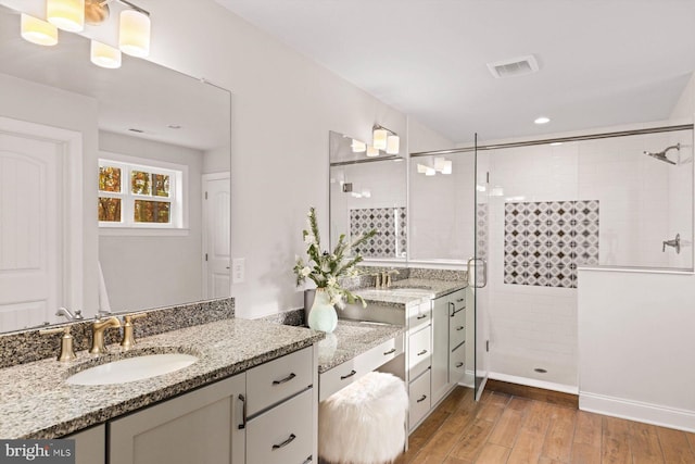 bathroom featuring a shower stall, wood finished floors, two vanities, and recessed lighting
