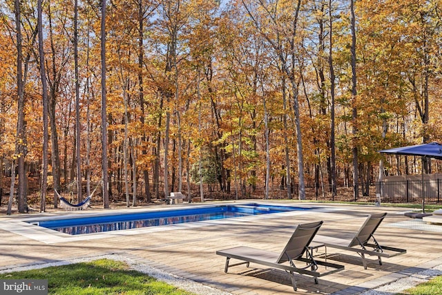 view of swimming pool with fence, a patio area, and a forest view