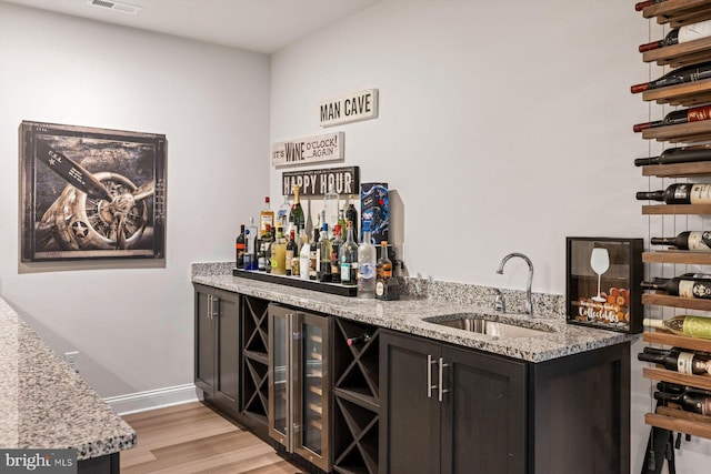 bar featuring wine cooler, light stone countertops, sink, and light hardwood / wood-style floors