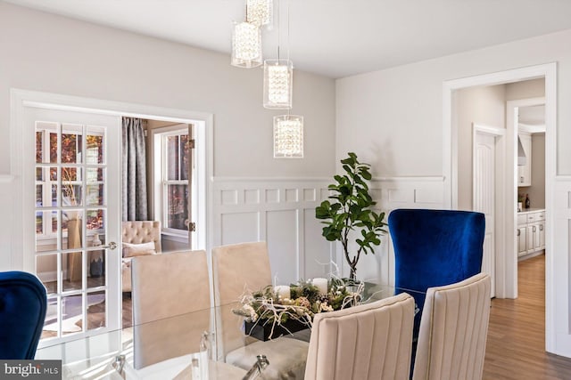 dining space featuring a decorative wall, wood finished floors, a wainscoted wall, and a chandelier