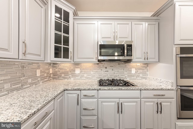 kitchen with light stone countertops, stainless steel appliances, white cabinetry, and tasteful backsplash