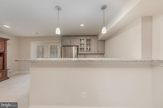 kitchen featuring light stone countertops, stainless steel fridge, light carpet, and decorative light fixtures