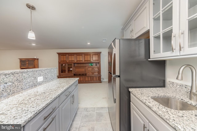 kitchen with white cabinets, decorative light fixtures, light stone counters, and sink