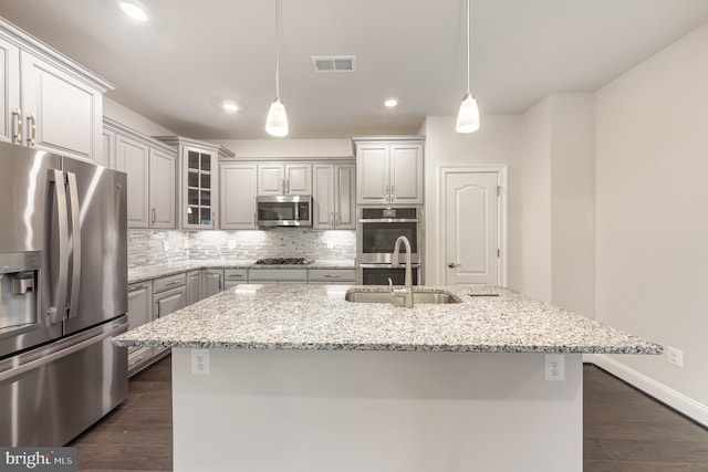 kitchen with light stone countertops, appliances with stainless steel finishes, a kitchen island with sink, and pendant lighting