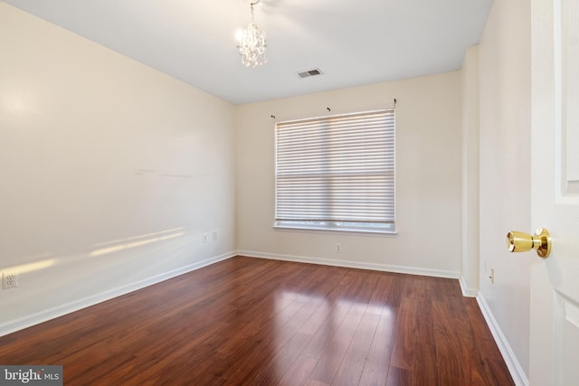 empty room with dark hardwood / wood-style flooring and an inviting chandelier