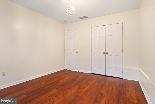 unfurnished bedroom featuring dark hardwood / wood-style floors, a closet, and a notable chandelier