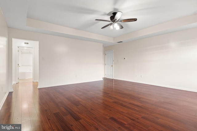 empty room featuring ceiling fan, a raised ceiling, and dark hardwood / wood-style flooring